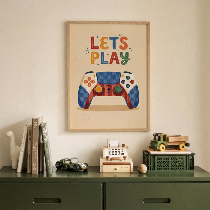 a framed poster with the text "LET'S PLAY" above a colorful illustration of a video game controller, which is displayed on a wall above a green dresser. The dresser has various items on it, including a toy car, a toy truck, and a small toy cash register.
