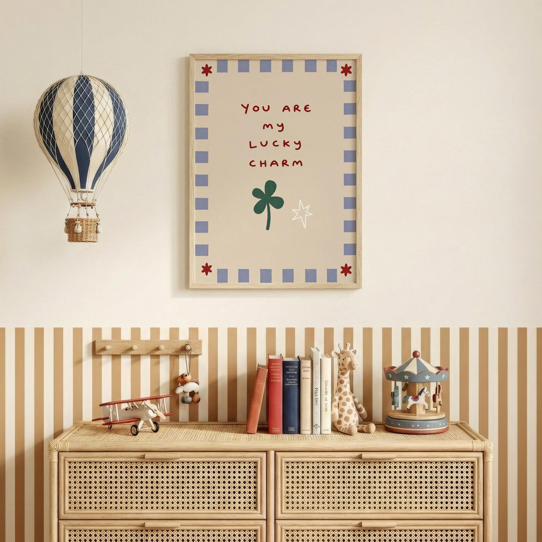 a wall with a framed poster that reads "You are my lucky charm" and a hot air balloon hanging above it. Below the poster, there is a wooden dresser with a carousel and a collection of books.