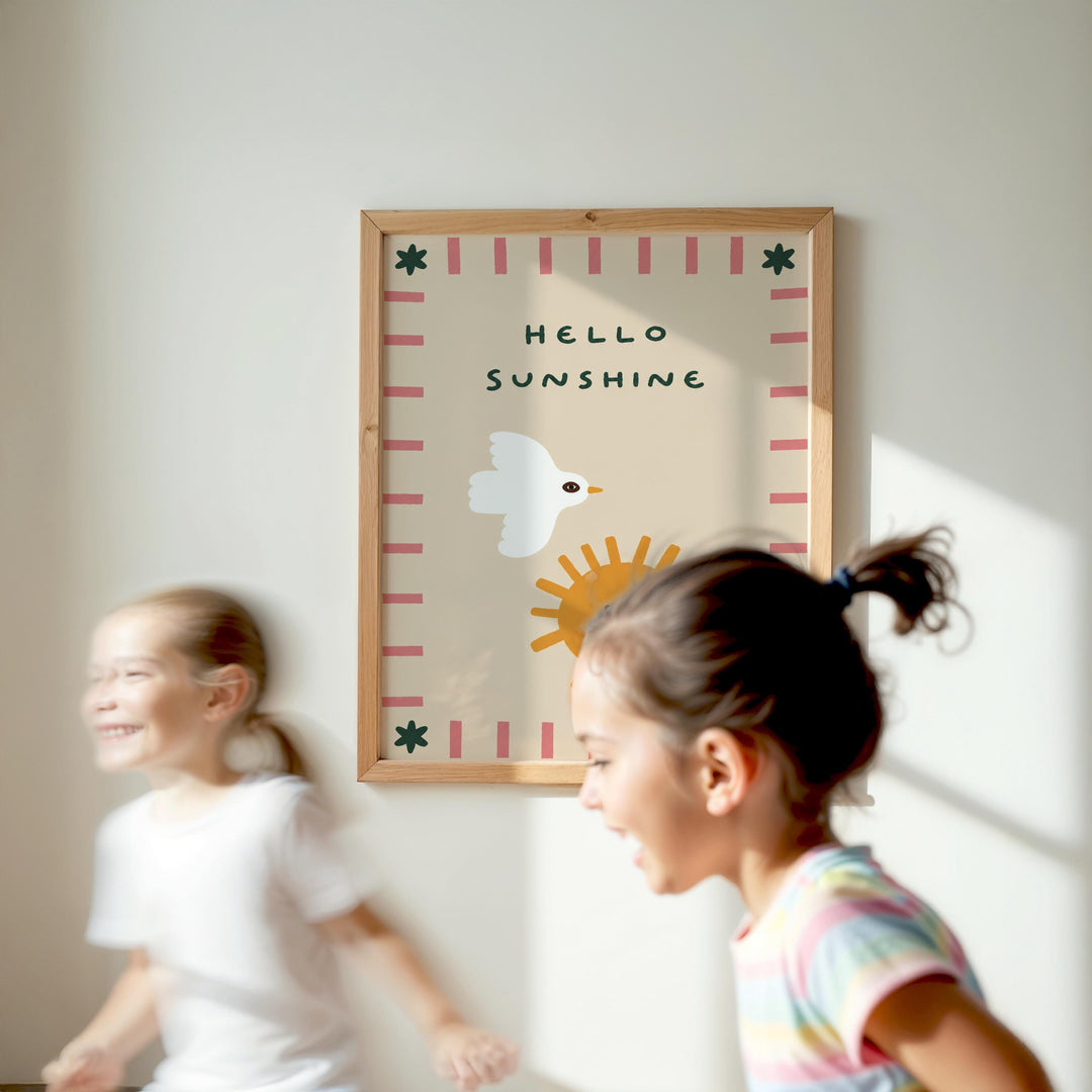 Two young girls are running in front of a framed poster with the text "Hello Sunshine" on a white wall.