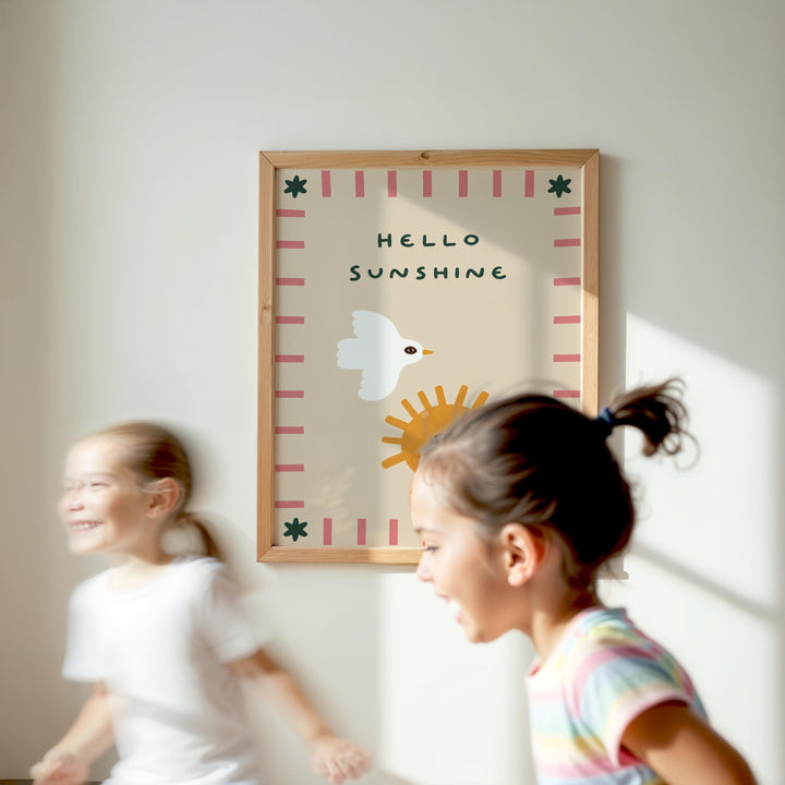 Two young girls are running in front of a framed poster with the text "Hello Sunshine" on a white wall.