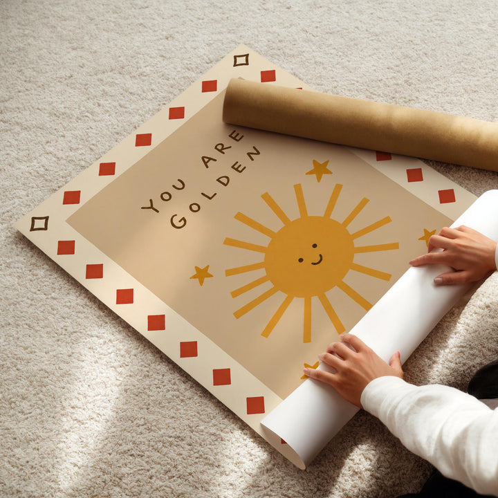 A person's hands are holding a roll of paper, which appears to be a poster or artwork, with a sun and star design on it.