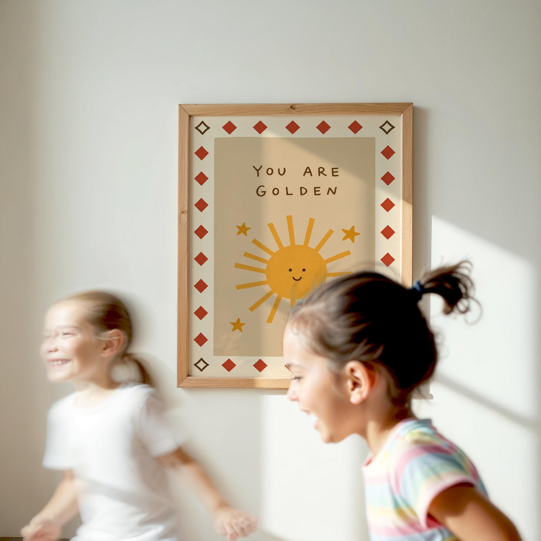 Two young girls are running in front of a framed poster with a sun and stars design, which says "You are Golden".