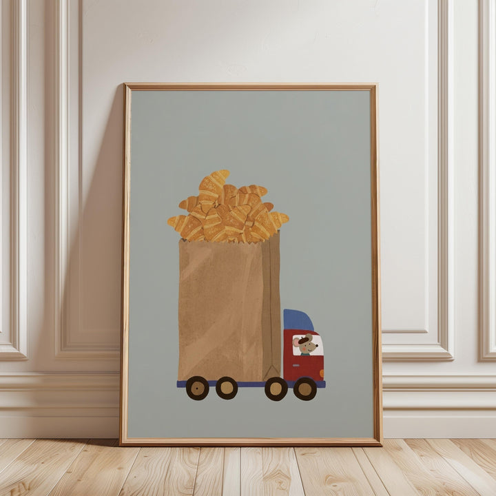 A framed illustration depicting a truck carrying a large bag filled with golden-brown pastries, likely croissants, against a light blue background.