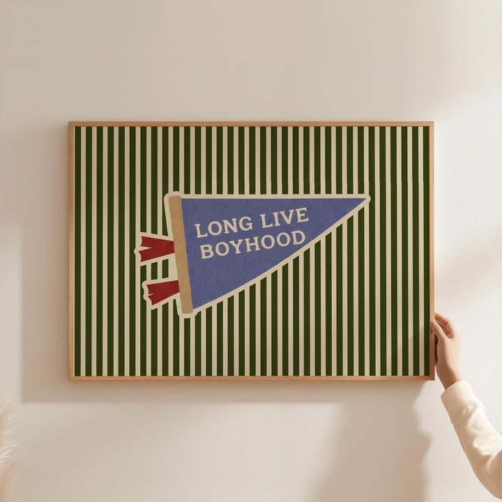 A framed poster with a green and white striped background and a blue triangular flag with the text "LONG LIVE BOYHOOD" displayed on it.