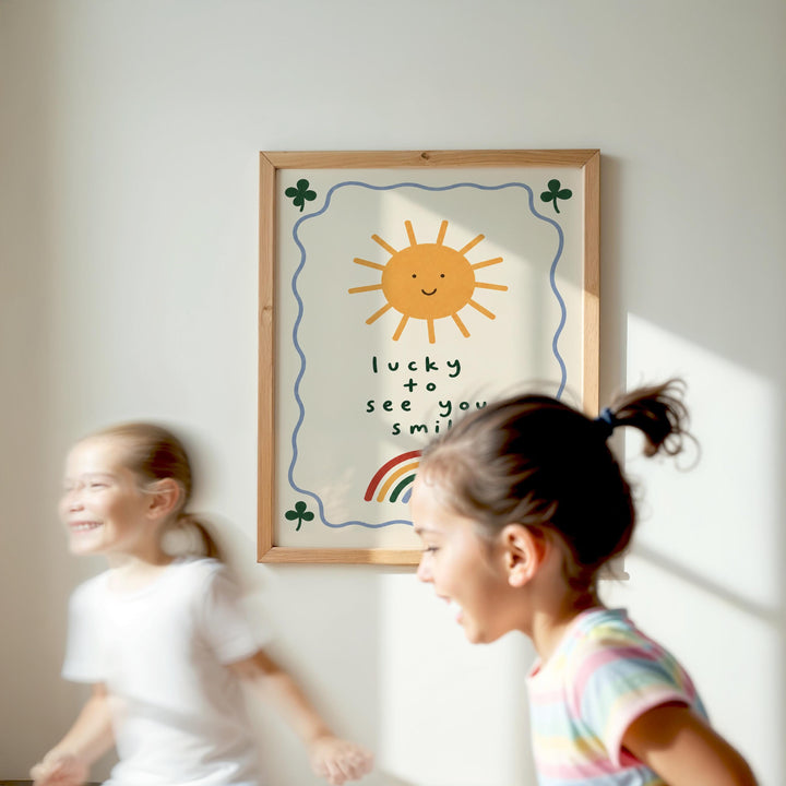 Two young girls are running in front of a framed poster with a sun and rainbow design, which says "lucky to see you smile".