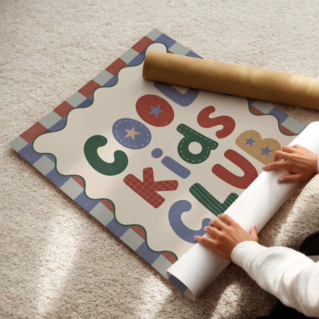 A child's hands are seen placing a roll of paper on a colorful poster that displays the text "Cool Kids Club".