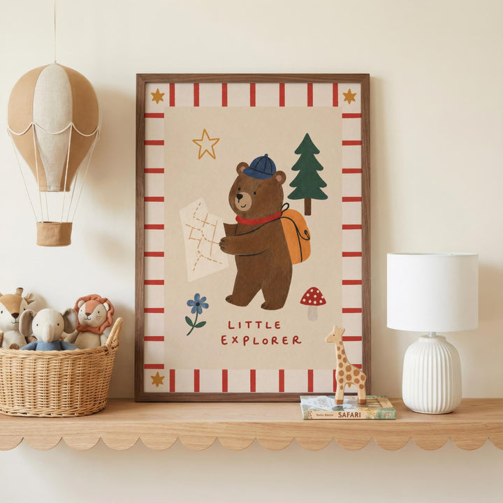 a framed picture of a bear holding a map, with the words "Little Explorer" written below it. The bear is wearing a hat and backpack, and there are other stuffed animals and toys in the background. The picture is displayed on a shelf, and there is a hot air balloon and a lamp in the scene.