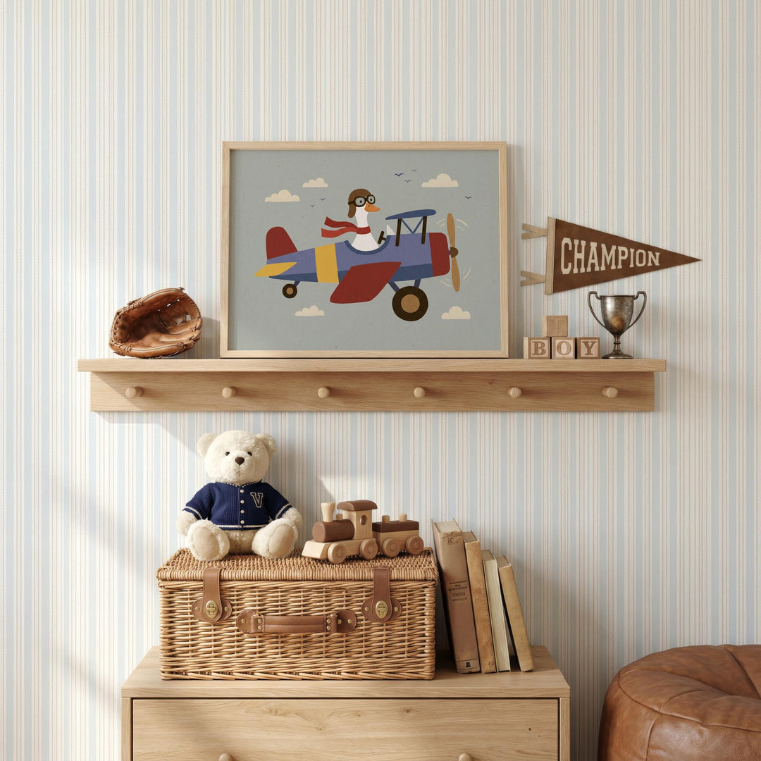 a child's bedroom with a shelf displaying a framed picture of a penguin piloting a biplane, a trophy, and a teddy bear. The shelf also holds a wicker basket, a wooden toy train, and a collection of books.