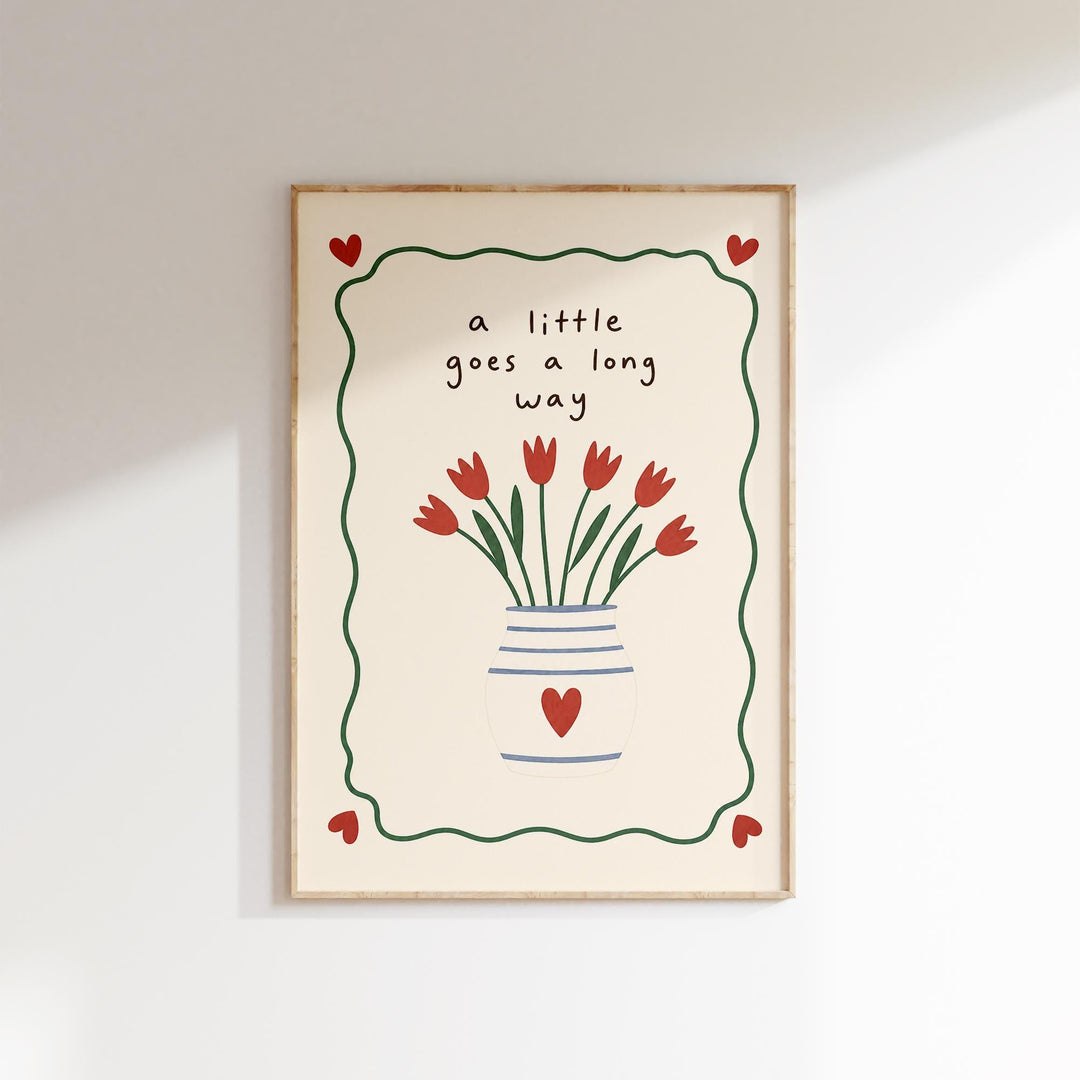 A framed print with a vase of red flowers and the text "a little goes a long way" written on it.