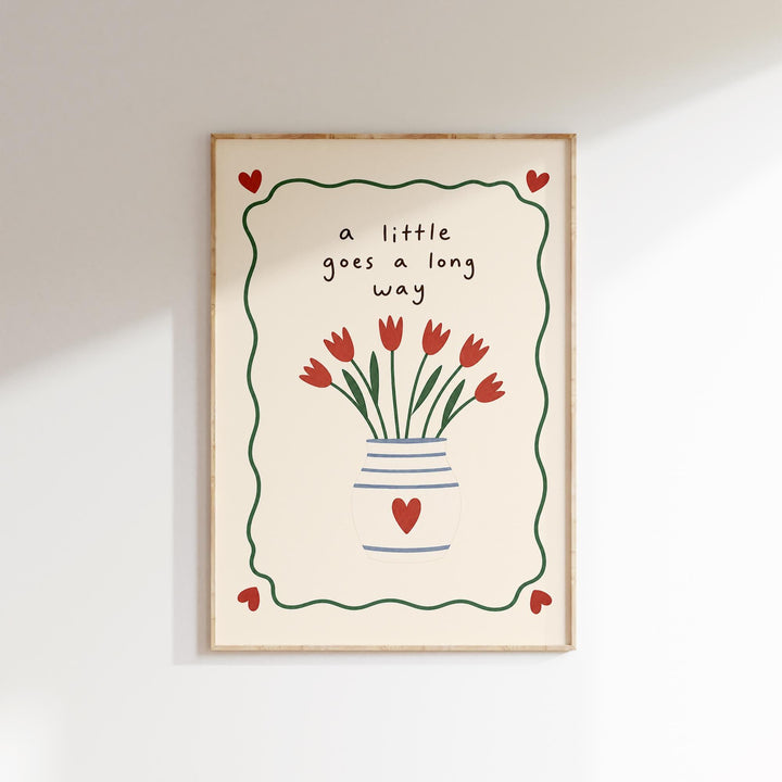 A framed print with a vase of red flowers and the text "a little goes a long way" written on it.