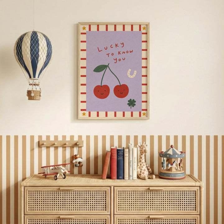 a wall with a framed poster of cherries and a hot air balloon, along with a wooden dresser below it. The dresser has a collection of books and toys on top of it.