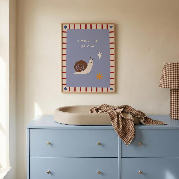 a blue dresser with a white sink on top, and a framed poster with a snail and the text "Take it slow" hanging on the wall above the dresser.