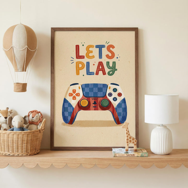 a framed poster with a colorful illustration of a video game controller, accompanied by the text "LET'S PLAY" in a playful font. The poster is displayed on a shelf, with a basket of stuffed animals and a lamp nearby.