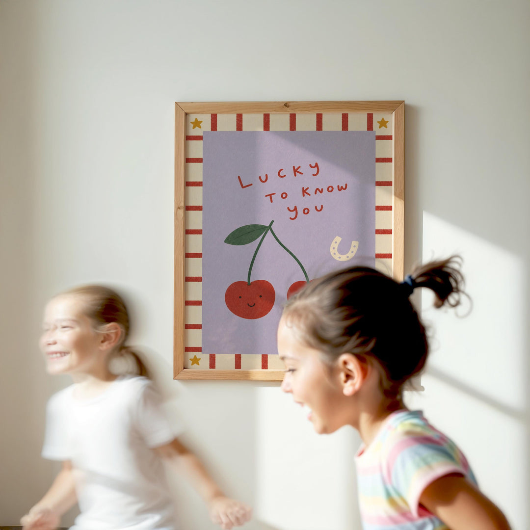 Two young girls are running in front of a framed poster with a cherry and the text "Lucky to know you".