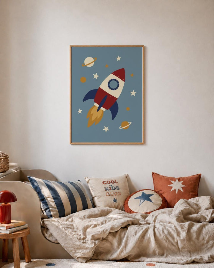 a framed artwork of a rocket ship flying through a space scene, with planets and stars in the background. The artwork is hanging on a wall above a bed with striped pillows and a star-patterned pillow.
