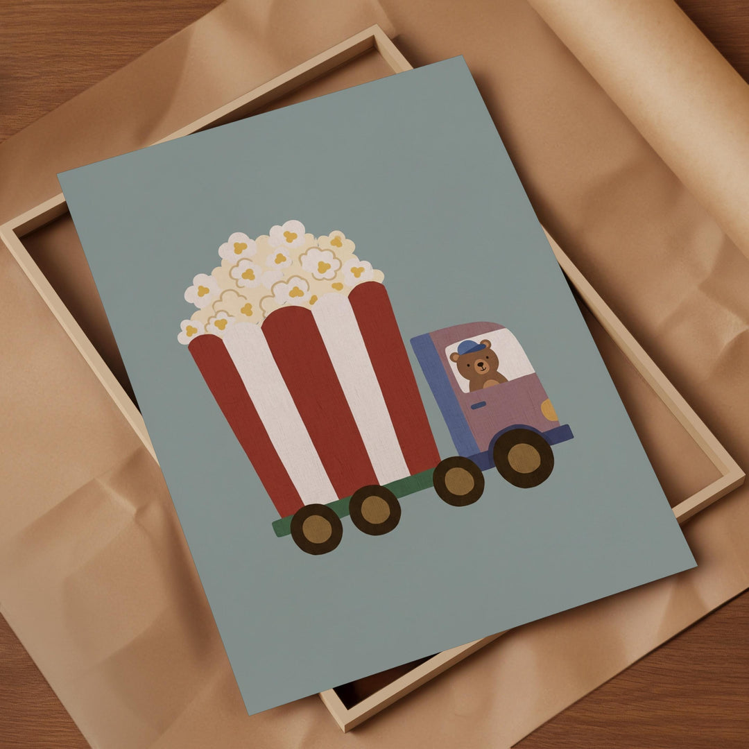 A framed illustration of a cartoon truck carrying a large bucket of popcorn, with a teddy bear inside the truck.