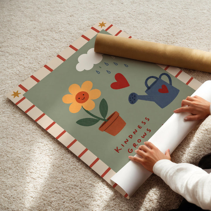 A child's hands are seen rolling up a poster with a colorful design featuring a flower, a watering can, and a heart.