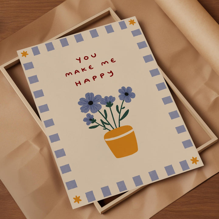 A greeting card with a floral design and the text "You make me happy" is displayed on a wooden surface.