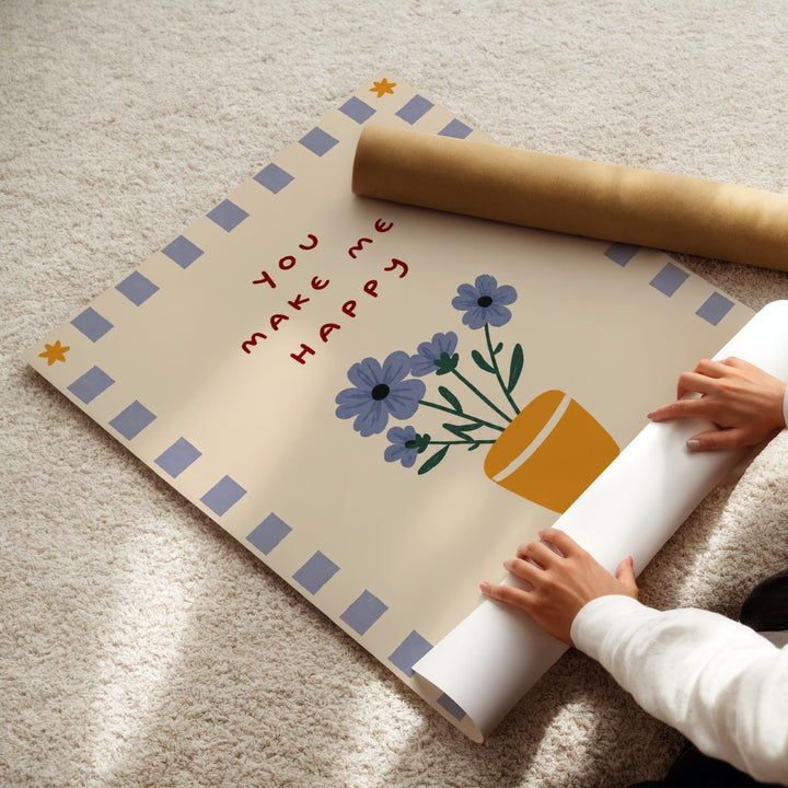 A person's hands are rolling up a poster with a floral design and the text "You make me happy" on it.