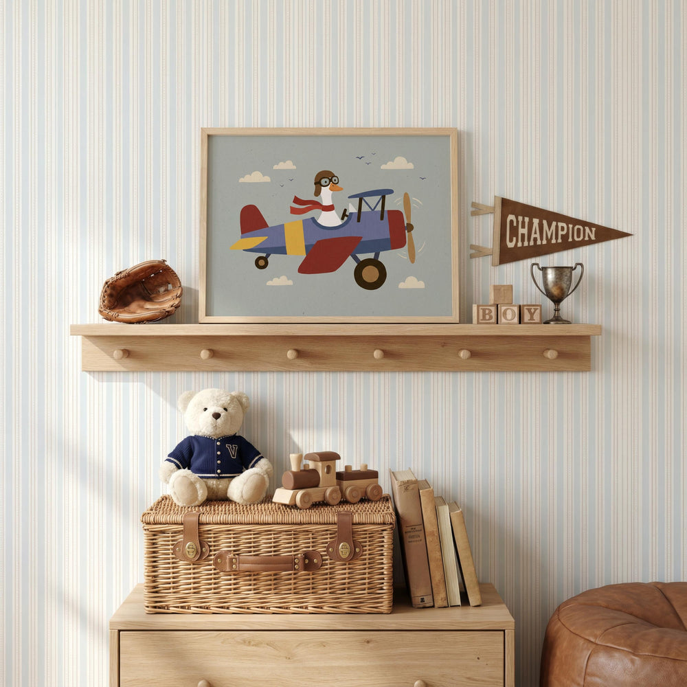a child's bedroom with a shelf displaying a framed picture of a penguin piloting a biplane, a trophy, and a teddy bear. The shelf also holds a wicker basket, a wooden toy train, and a collection of books.