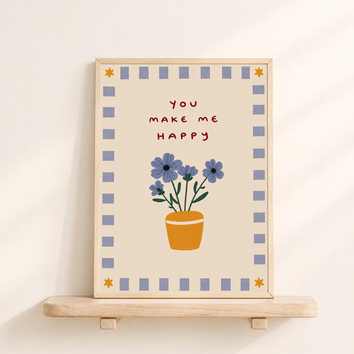 A framed picture with a floral design and the text "You make me happy" on it, displayed on a wooden shelf against a white wall.