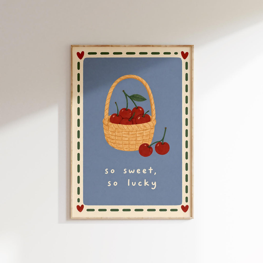 A framed illustration of a basket filled with cherries, accompanied by the text "so sweet, so lucky" in a playful, whimsical style.