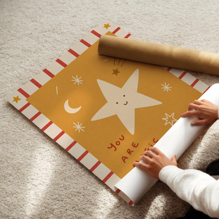 A person's hands are rolling up a piece of paper with a star and moon design, which appears to be a decorative item or artwork.