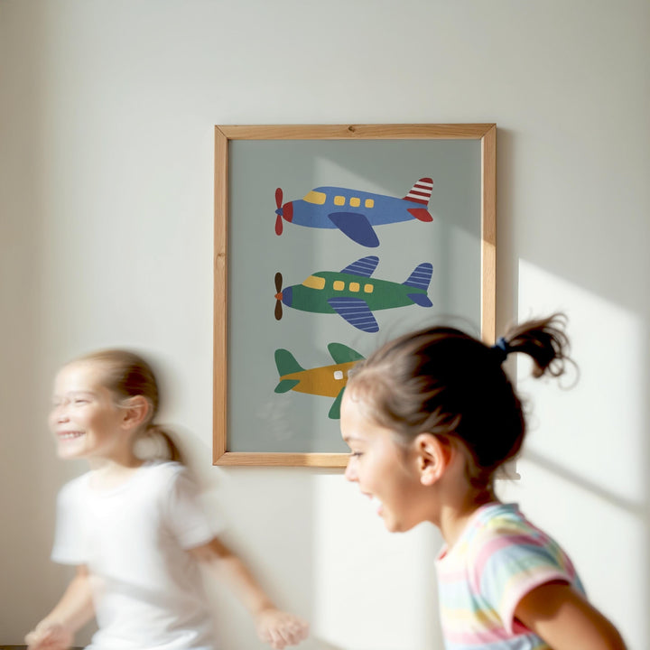 Two young girls are running in a room with a framed picture of colorful airplanes hanging on the wall.