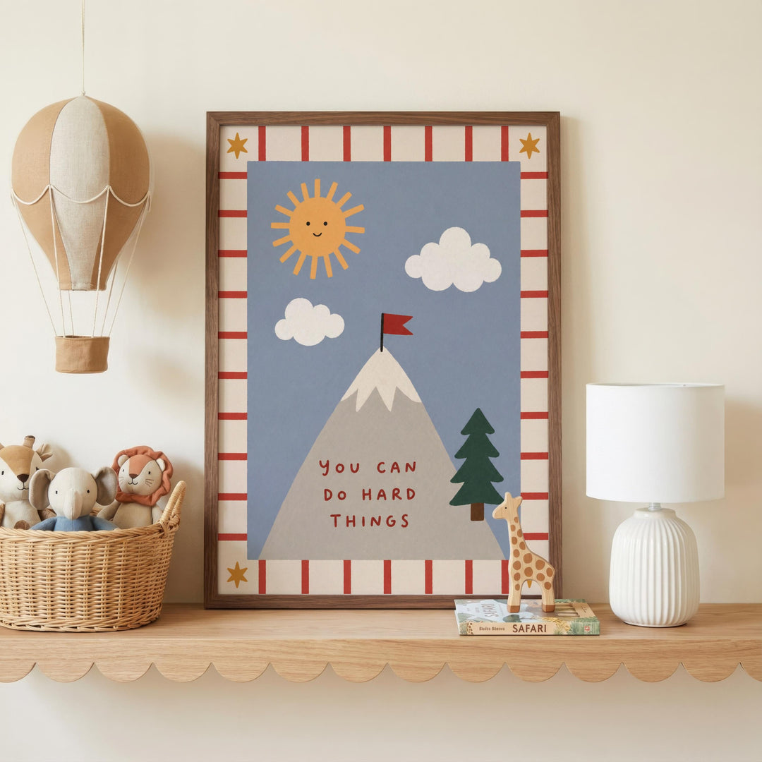 a framed poster with a mountain, a sun, clouds, and a flag, along with a motivational message. The poster is displayed on a shelf, accompanied by a basket of stuffed animals, a lamp, and a small toy giraffe.