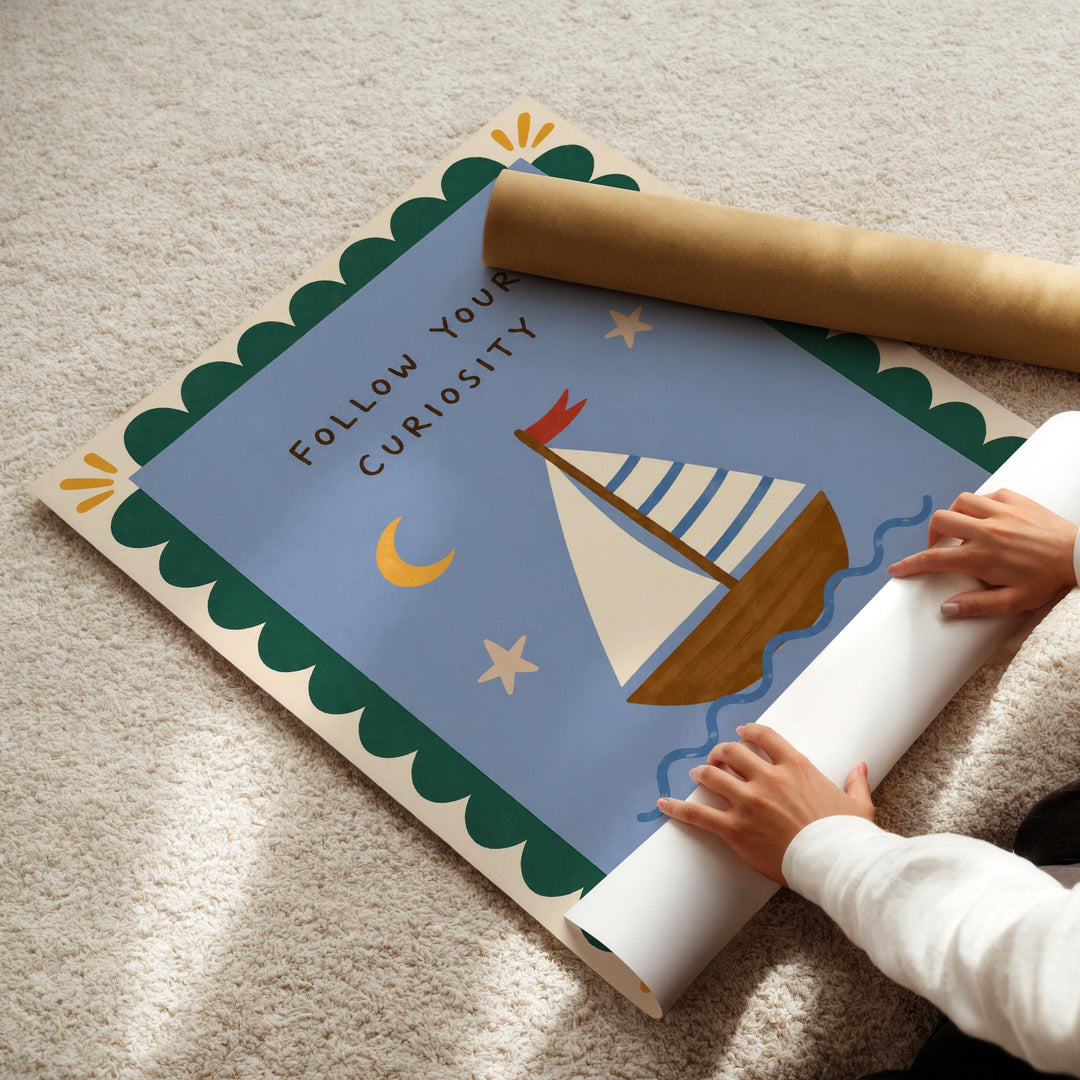 A child's hands are rolling up a poster with a sailboat illustration and the text "Follow Your Curiosity" on it.