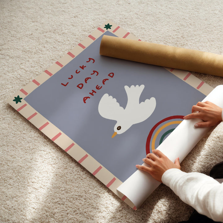 A person's hands are rolling up a poster with a white bird and a rainbow on it, which is placed on a carpeted floor.