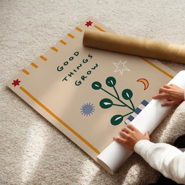 A person's hands are rolling up a poster with the text "Good Things Grow" on it, which appears to be a decorative piece.