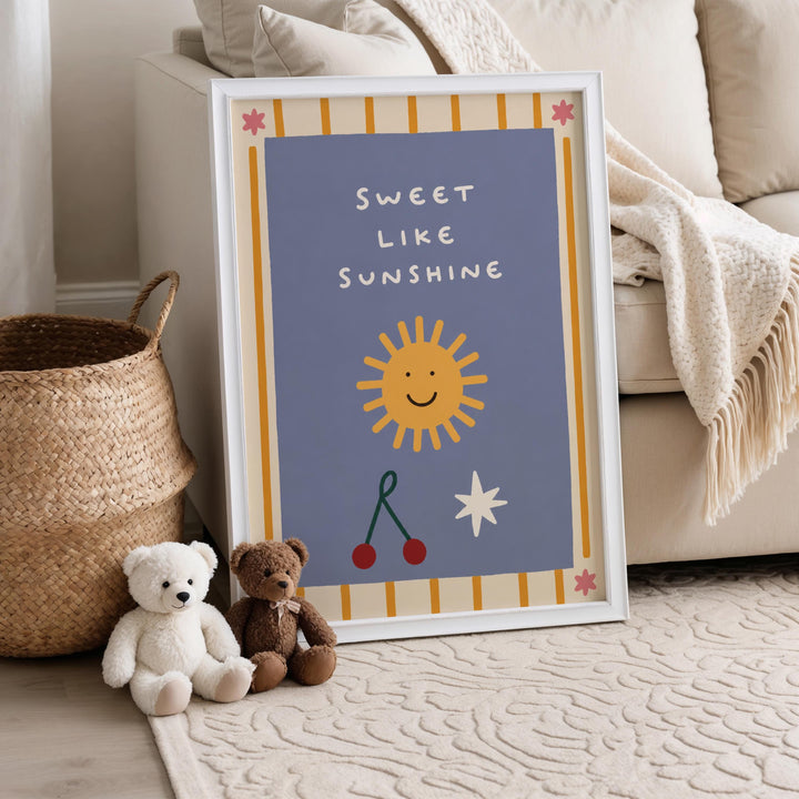 a framed poster with a cheerful design, including a sun, a smiling face, and a star, placed on a beige carpet next to a white couch. There are two teddy bears sitting on the floor in front of the poster.