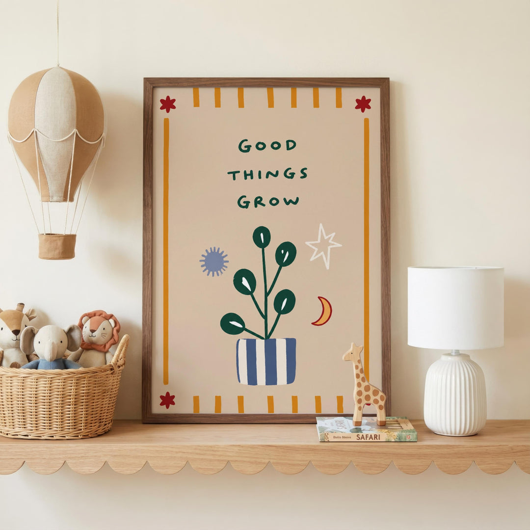 a framed poster with the text "GOOD THINGS GROW" on it, surrounded by various decorative elements such as a hot air balloon, a plant, and a giraffe figurine. The poster is displayed on a shelf, with a basket of stuffed animals and a lamp nearby.