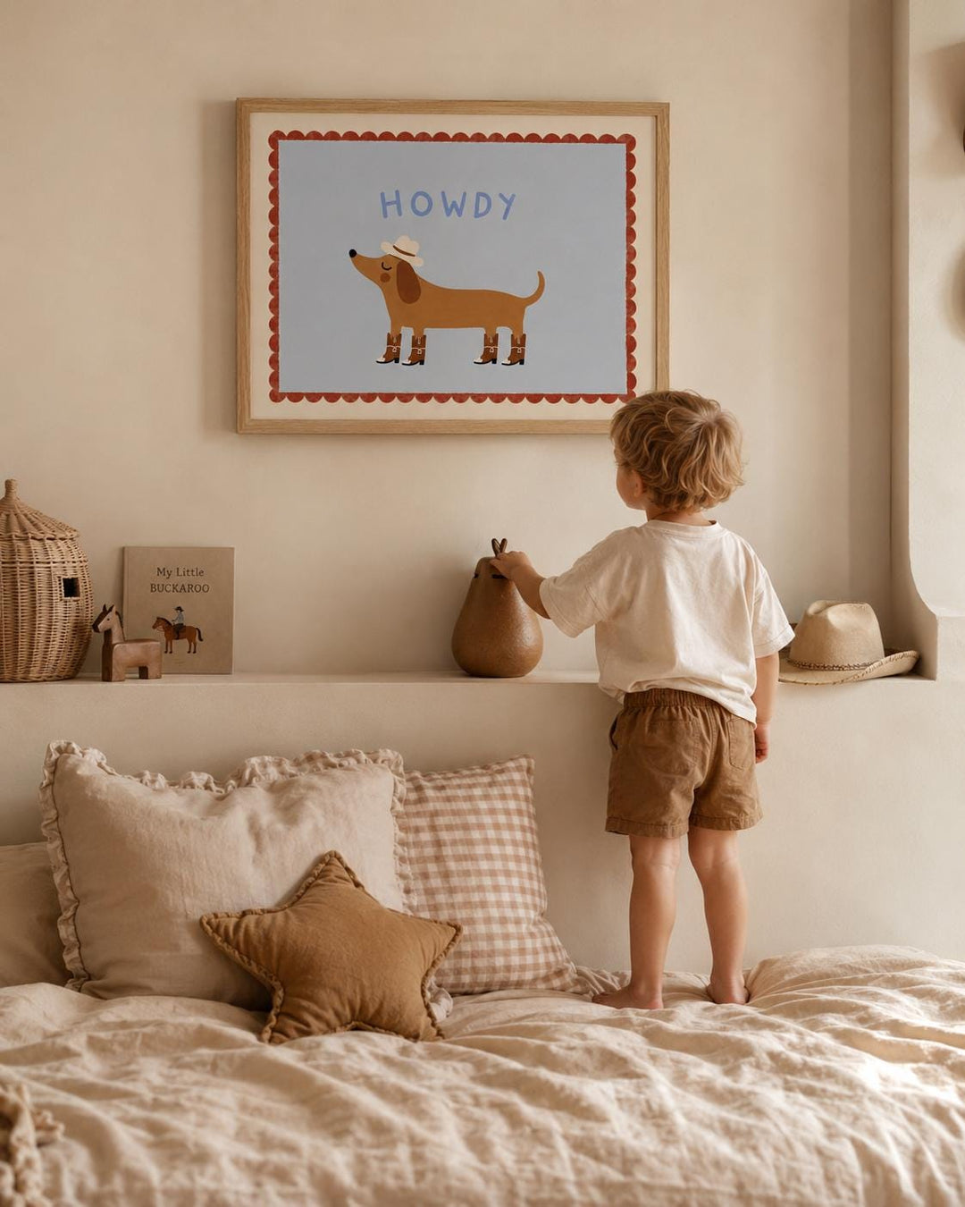 A young child standing on a bed, looking up at a framed picture of a cartoon dog.