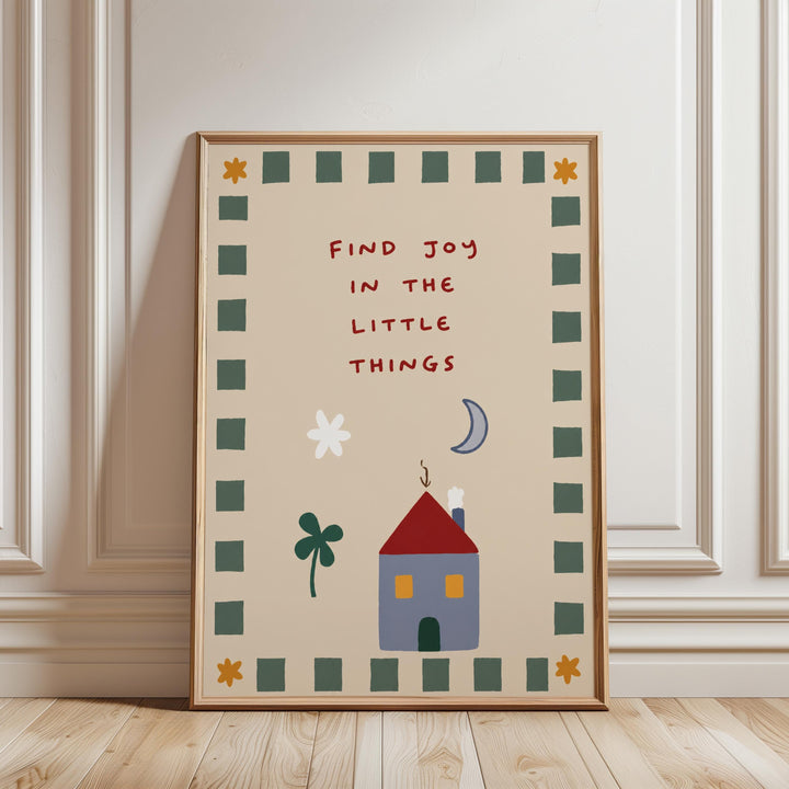The image is a framed poster with a whimsical illustration of a house, flowers, and a crescent moon, along with the text "Find Joy in the Little Things" written in a playful font.