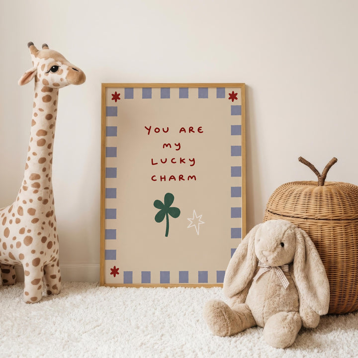 a giraffe and a stuffed rabbit, with a framed sign that reads "You are my lucky charm" placed between them on a white carpet.