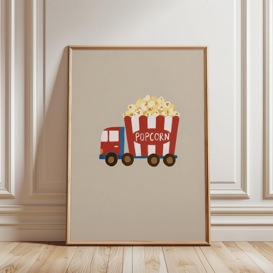 A framed illustration of a red and white popcorn truck with the word "POPCORN" on the side, parked on a wooden floor against a white wall.