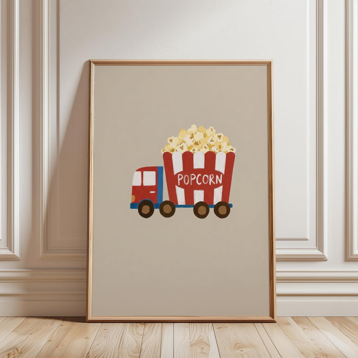 A framed illustration of a red and white popcorn truck with the word "POPCORN" on the side, parked on a wooden floor against a white wall.