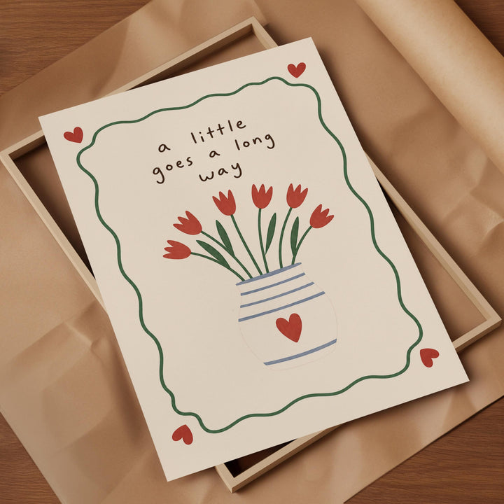 A greeting card with a vase of red flowers and the text "a little goes a long way" written on it.