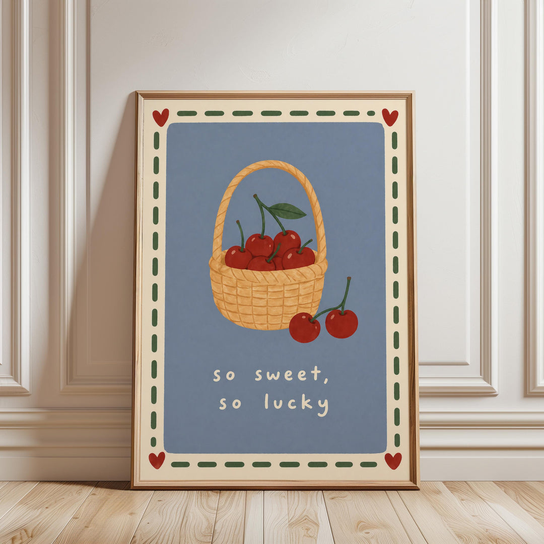 A framed illustration of a basket filled with cherries, accompanied by the text "so sweet, so lucky" in a decorative border.