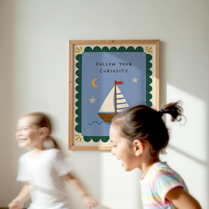 Two young girls are running in front of a framed poster with a sailboat and the text "Follow Your Curiosity" on a white wall.