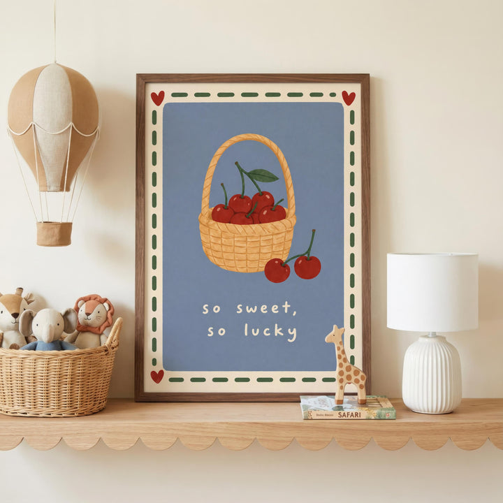 a framed poster with a basket of cherries and the text "so sweet, so lucky" on a shelf, accompanied by a toy giraffe and a hot air balloon.