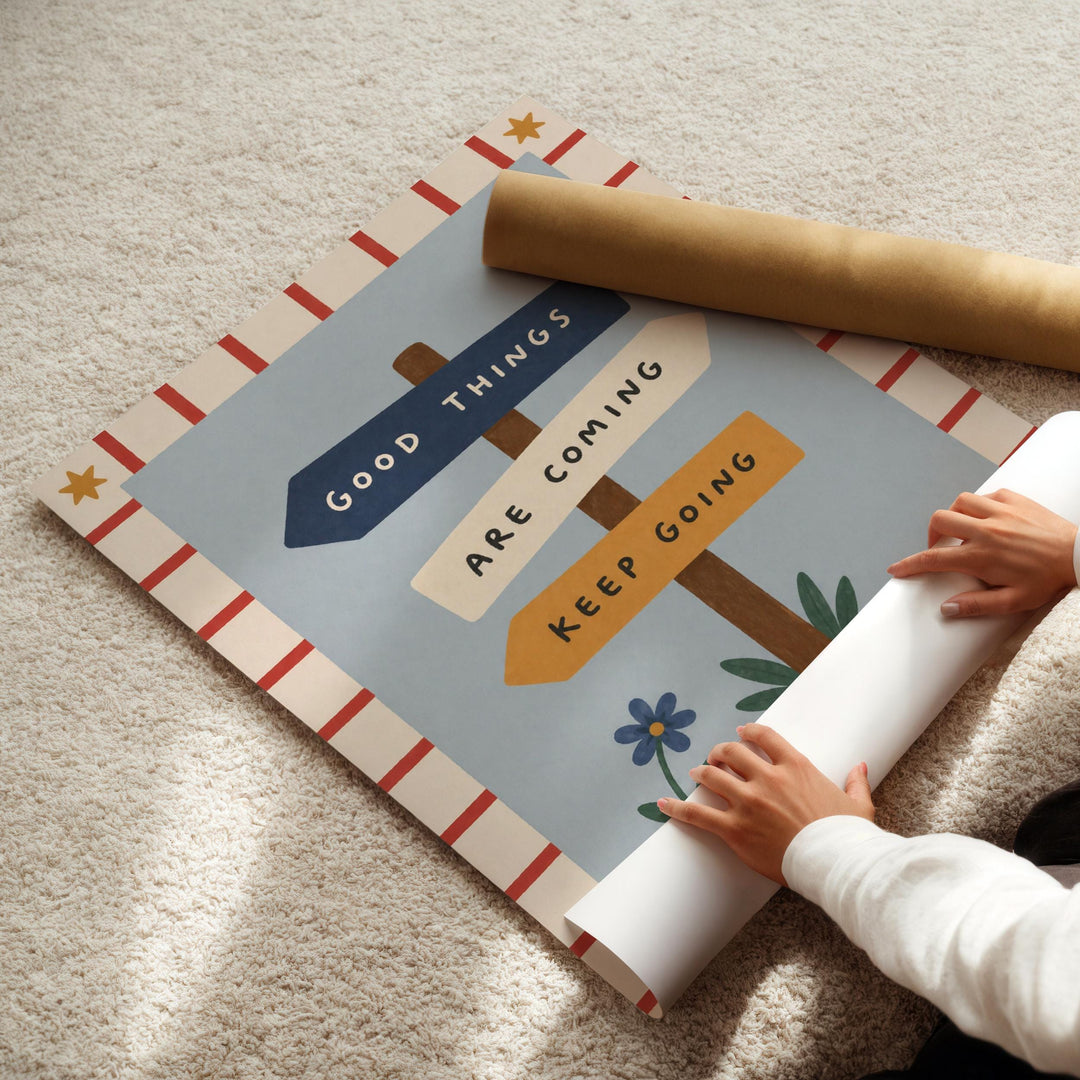 A person's hands are rolling up a poster with the text "Good Things Are Coming" and "Keep Going" on it.