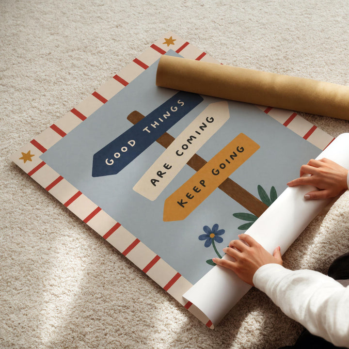 A person's hands are rolling up a poster with the text "Good Things Are Coming" and "Keep Going" on it.