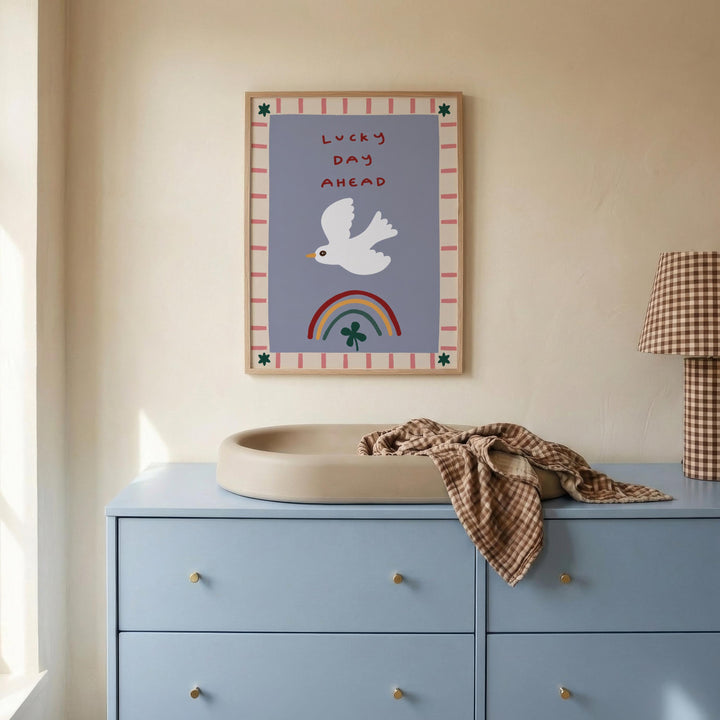 a blue dresser with a white sink on top, and a framed poster with a white bird and a rainbow above it. The poster has the text "Lucky day ahead" written on it.