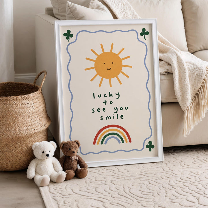 A framed poster with a sun and rainbow design, along with the text "lucky to see you smile" is displayed on a wall, accompanied by two stuffed teddy bears sitting on the floor.
