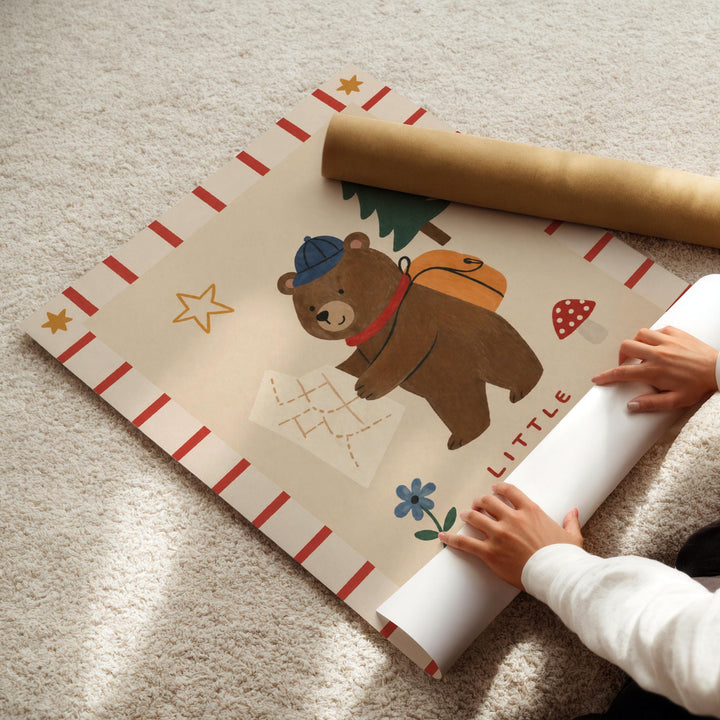 A child's hands are holding a roll of paper with a colorful bear illustration on it, which appears to be a map or a travel-themed design.