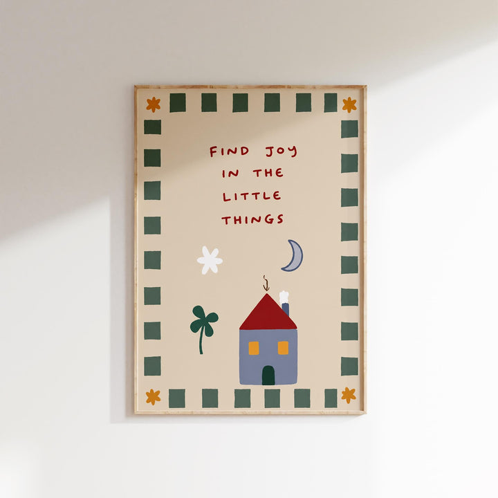 The image is a framed poster with a cheerful and whimsical design. It features a house, flowers, and a crescent moon, all set against a light brown background. The text on the poster reads "Find Joy in the Little Things", which appears to be a message or quote about finding happiness in everyday moments.