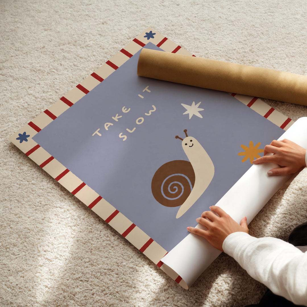 A person's hands are rolling up a piece of paper with a snail illustration and the text "Take it slow" written on it.